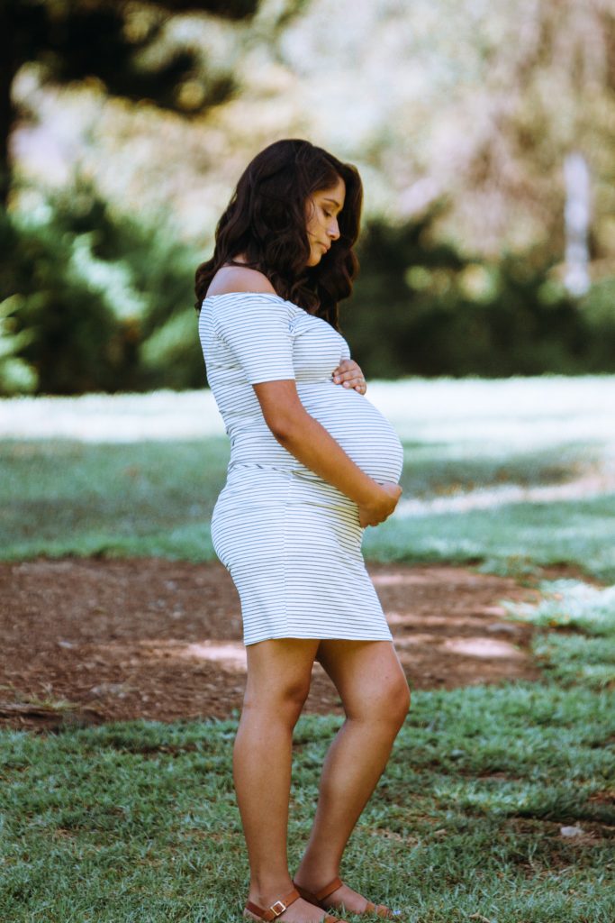 Femme enceinte en robe blanche, en train de tenir son ventre