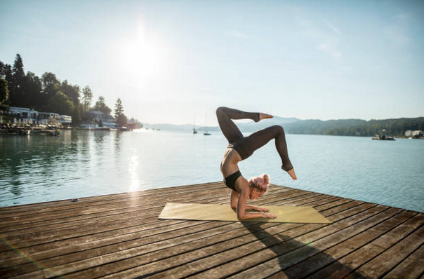 Femme qui réalise une posture complexe de yoga sur le ponton d'un lac