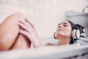 Femme profitant des bienfaits du son d'avoine dans son bain les yeux fermés en écoutant de la musique