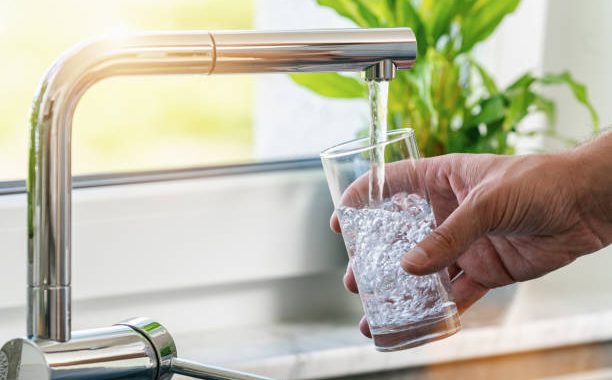Personne qui se sert un verre d'eau au robinet
