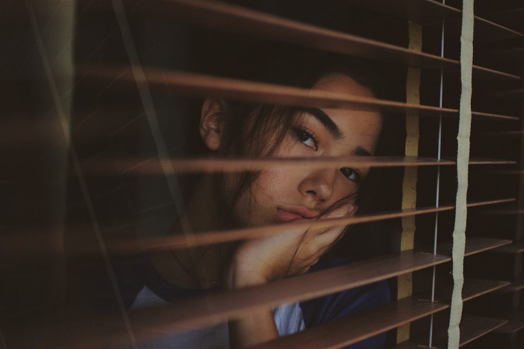 Jeune fille qui regarde par la fenêtre, une main dans son visage en signe d'ennui