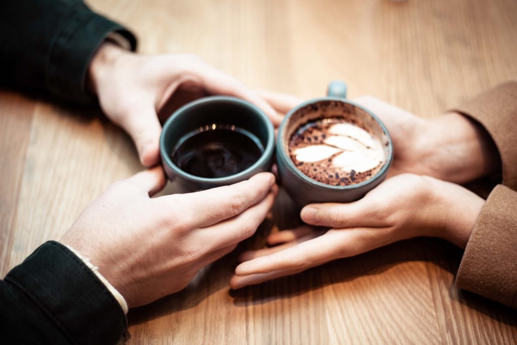 Gros plan sur les mains de deux personnes qui tiennent une tasse de café au centre de la table